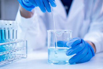 Closeup scientist hand using stirring rod for stirring blue liquid solution glass beaker chemical...