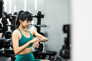 Fototapeta na wymiar Asian sportswoman is using sports smart watch in gym. 