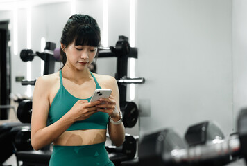 Asian woman working out in gym is using mobile phone. 