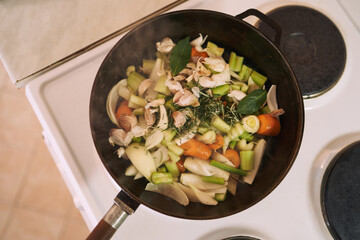 Raw chopped vegetables are stewed in a frying pan on the stove. Top view