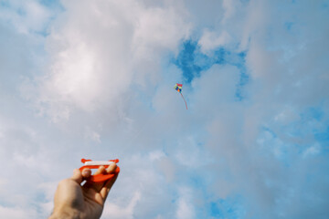 Spool of thread with a kite flying in a cloudy sky in a man hand