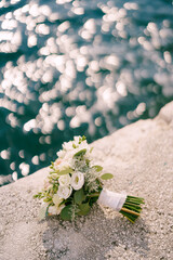 Bridal bouquet lies on a stone border near the shining water