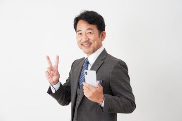 スマートフォンを持ってピースサインをする中年のビジネスマン　白背景
