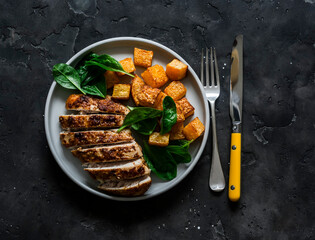 Baked chicken breast, pumpkin and spinach - a delicious healthy lunch on a dark background, top view