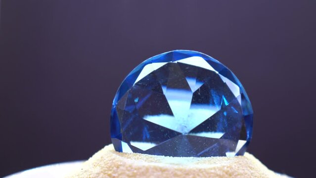 Closeup footage of blue diamond shape glass crystal paperweight on sand slowly rotating