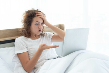 Fototapeta premium Young beautiful business woman has headache working with laptop while lying in bed in the morning after waking up.