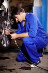 Mechanic, man and change wheel in shop, electric drill and car service or auto repairs for...