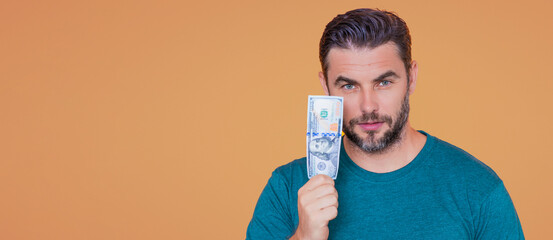 Handsome man holding money isolated over beige studio, banner. Money in dollar banknotes. Pile of...