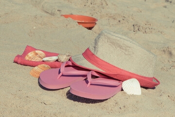 Straw hat, slippers and towel on sand at beach. Accessories for relax in summer