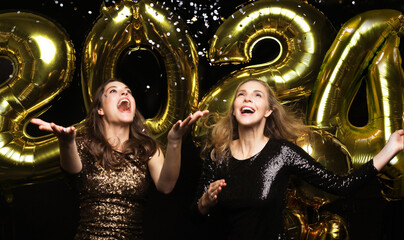 Happy gorgeous girls in stylish sexy party dresses holding gold 2021 balloons, having fun at New...