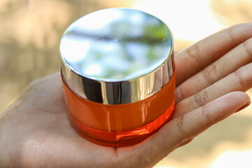 hand holding a luxury cosmetic product in nature, 4oz jar mockup with silver lid