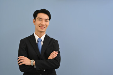 Obraz na płótnie Canvas Waist up portrait of a Confident Young Asian Businessman in a formal suit standing with arms crossed gesture over a color isolated studio background