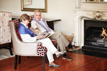 Senior couple, relax and reading by fire place on holiday, retirement or vacation together at hotel...