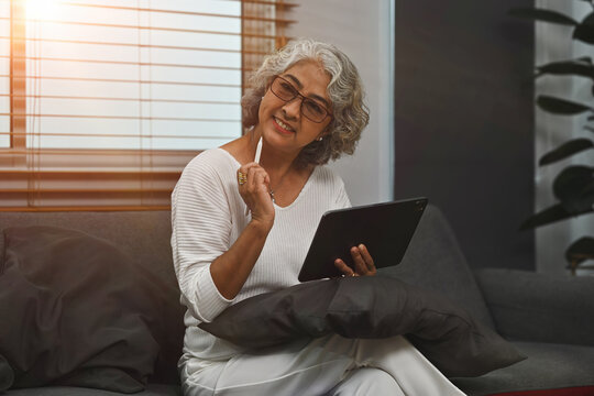 Portrait image of an Old Asian woman using a digital tablet while sitting on the sofa. Elderly people and digital technology concepts