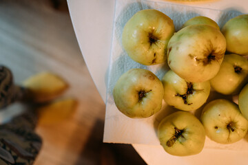 In the foreground, whole yellow apples are lying on the table. There are blurred legs in the background. Harvest from your own garden