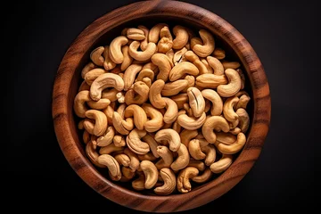 Fotobehang top view of a wooden bowl full of cashew nuts on black background © Rangga Bimantara