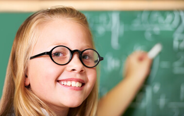 Portrait, nerd and happy kid writing on chalkboard in class for learning, education and study math. Face, glasses and smile of geek at school, cute girl child and student in classroom in Australia