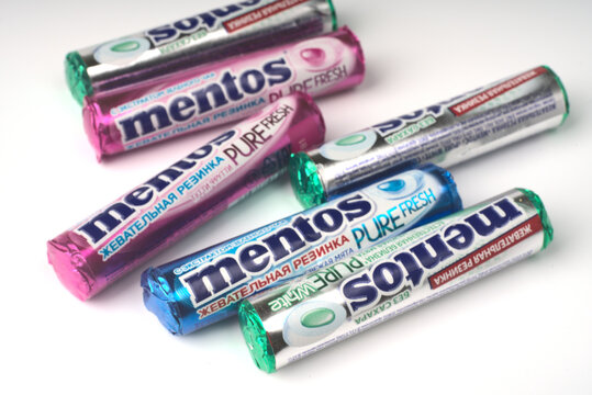 Moscow, Russia - june 18 2021: Many packages of Mentos gum and next to it the round gum itself on a white closeup background. Space for the text
