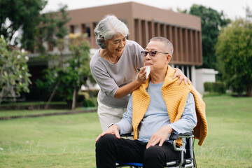 Asian Senior couple sitting in wheelchairs taking care of each other.in romantic time They laughing and smiling while sitting outdoor in park..