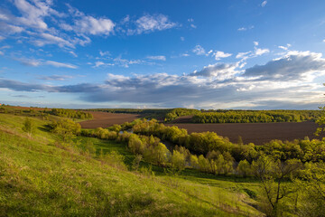 View from the hill to plowed farmland. Landscape with a river, arable land and green trees.