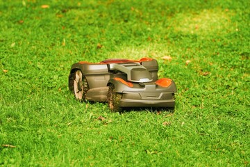 Fototapeta premium Robotic lawn mower on grass, side view. Close up isolated of automatic lawn mower. Smart lawn caring. Electronic grass trimmer.