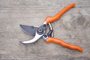 Pruning shears or scissors with orange handle on wooden background. Concept, tool, equipment for working in garden, Use for pruning branches of trees, bushes, or grass. Gardening and agriculture tool.