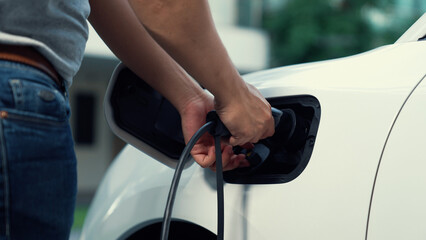 Progressive man attaches an emission-free power connector to the battery of electric vehicle at his...