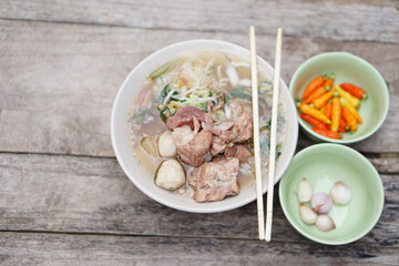Stewed Pork Soup with meat balls and vegetables in bowl, chopsticks on top, old wooden background. Concept, traditional food. Favorite menu that can cook or order in noodle foodshops in Thailand.     