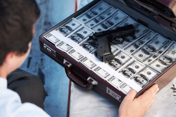 Businessman, gun and briefcase with money for crime, corruption, thief and fraud outdoor for...