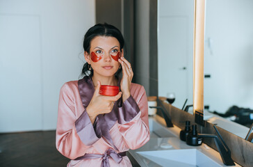 Brunette woman first time placing face cosmetic patches on face at bathroom at home. Cosmetics,...