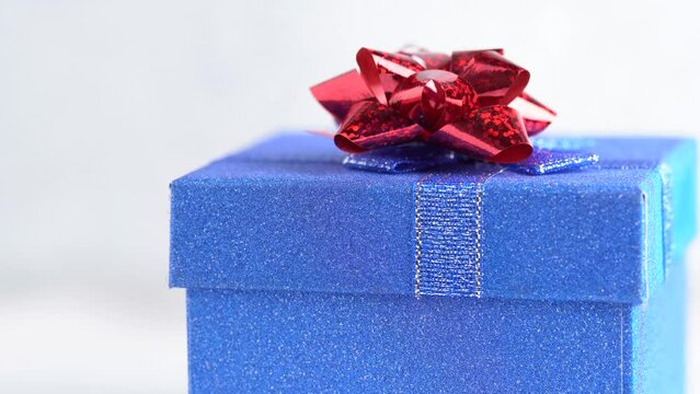 Glittering blue gift box with a red bow rotates. Gift concept or birthday party. Blue gift box, close up