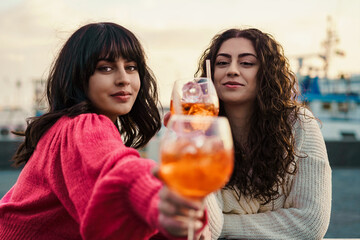 Friends toasting with spritz at the harbor - Two women share a serene moment by the harbor,...