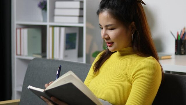 Young Asian woman at home writing diary notebook and doing homework.