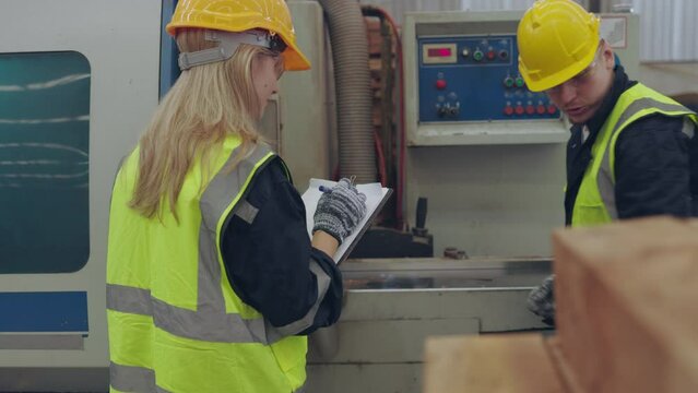 Female and male industrial engineers discussing safety checklist on clipboard in manufacturing factory.