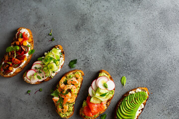 Healthy breakfast toasts with different toppings, avocado, salmon, cucumber, radish, cherry tomatoes and herbs. Copy space
