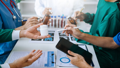 Medical team having a meeting with doctors in white lab coats and surgical scrubs seated at a table...