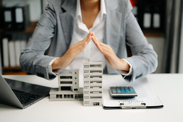 Female real estate agent is use hands to protect red roof for the concept of real estate investment about house trading, purchase at desk in office