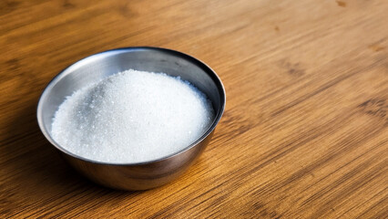 The pristine white sugar, with its sweet taste, rests in the container on the wooden-patterned floor.