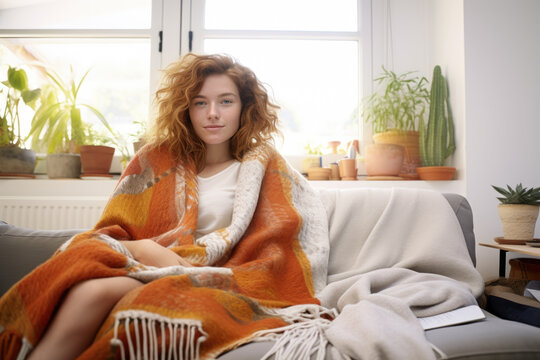 Young woman wrapped in a yellow blanket trying to warm up in the cold apartment