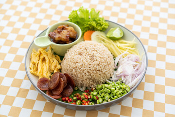 Rice mixed with shrimp paste sausage egg or chopped omelette fresh chili long beans onion mango cucumber carrot lettuce lemon and sweet streaky pork on banana leaf in dish on yellow table by thai food