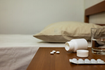 Sleeping pills on the nightstand next to the bed. Capsule bottle with glass of water.