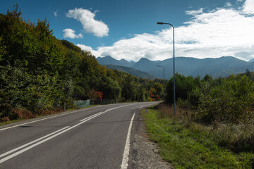 Natural landscape of road in forest on background of beautiful mountains and blue sky.