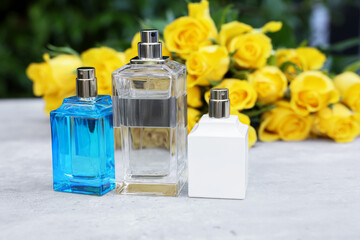 Perfumes and beautiful bouquet of yellow roses on light table outdoors, selective focus. Space for text