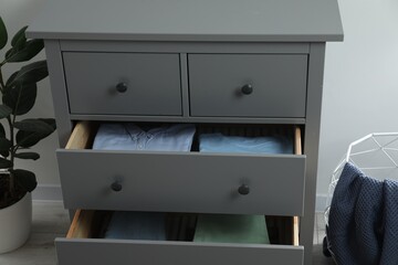 Sorting and organizing. Chest of drawers with different folded clothes indoors