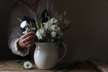 Obraz na płótnie Canvas Woman creating beautiful flower arrangement at wooden table, closeup. Space for text