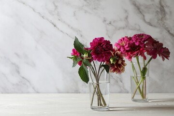 Bouquet of beautiful wild flowers and leaves in vases on white wooden table against marble background. Space for text