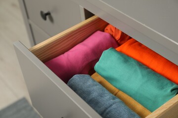 Different rolled shirts in drawer indoors. Organizing clothes