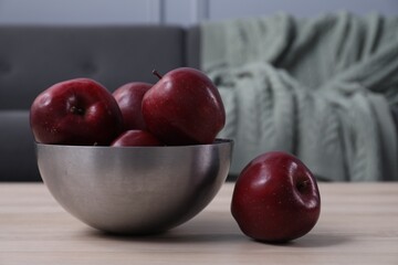 Red apples in bowl on wooden table indoors