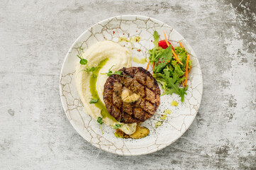 Juicy steak with mashed potatoes and greens on a gray background