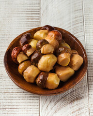 Canned porcini mushrooms in a wooden bowl on a white wooden background. Mushrooms, canned foods.